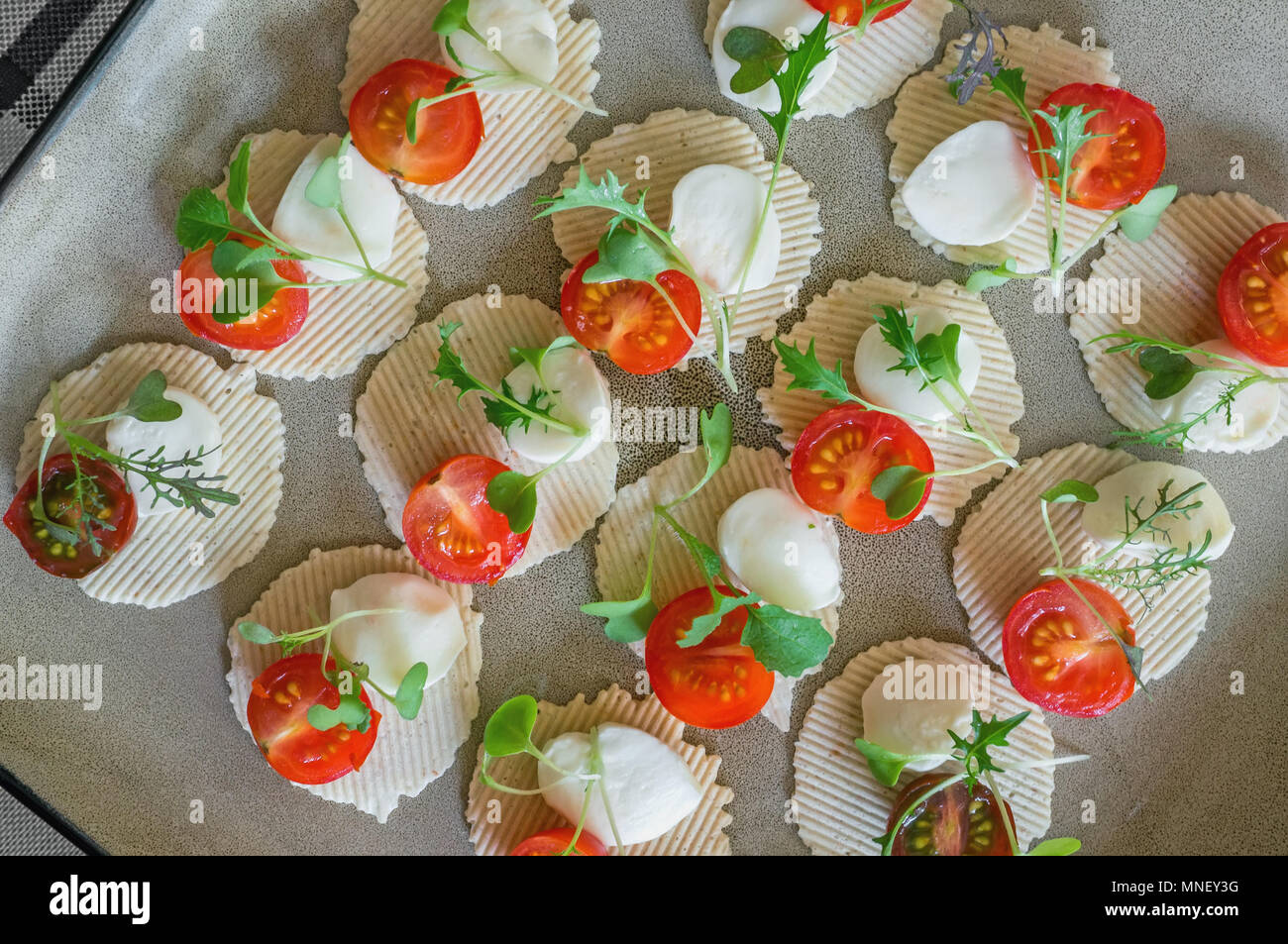 La mozzarella et tomates au thym, roquette et basilic sont sur les croustilles de maïs. Préparation des canapés. Close up. La vue d'en haut Banque D'Images