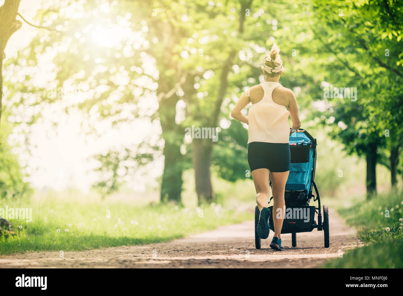 L'exécution de femme avec poussette de bébé profiter de journée d'été en parc. Le jogging ou la marche active avec la famille, supermaman baby jogger. Banque D'Images