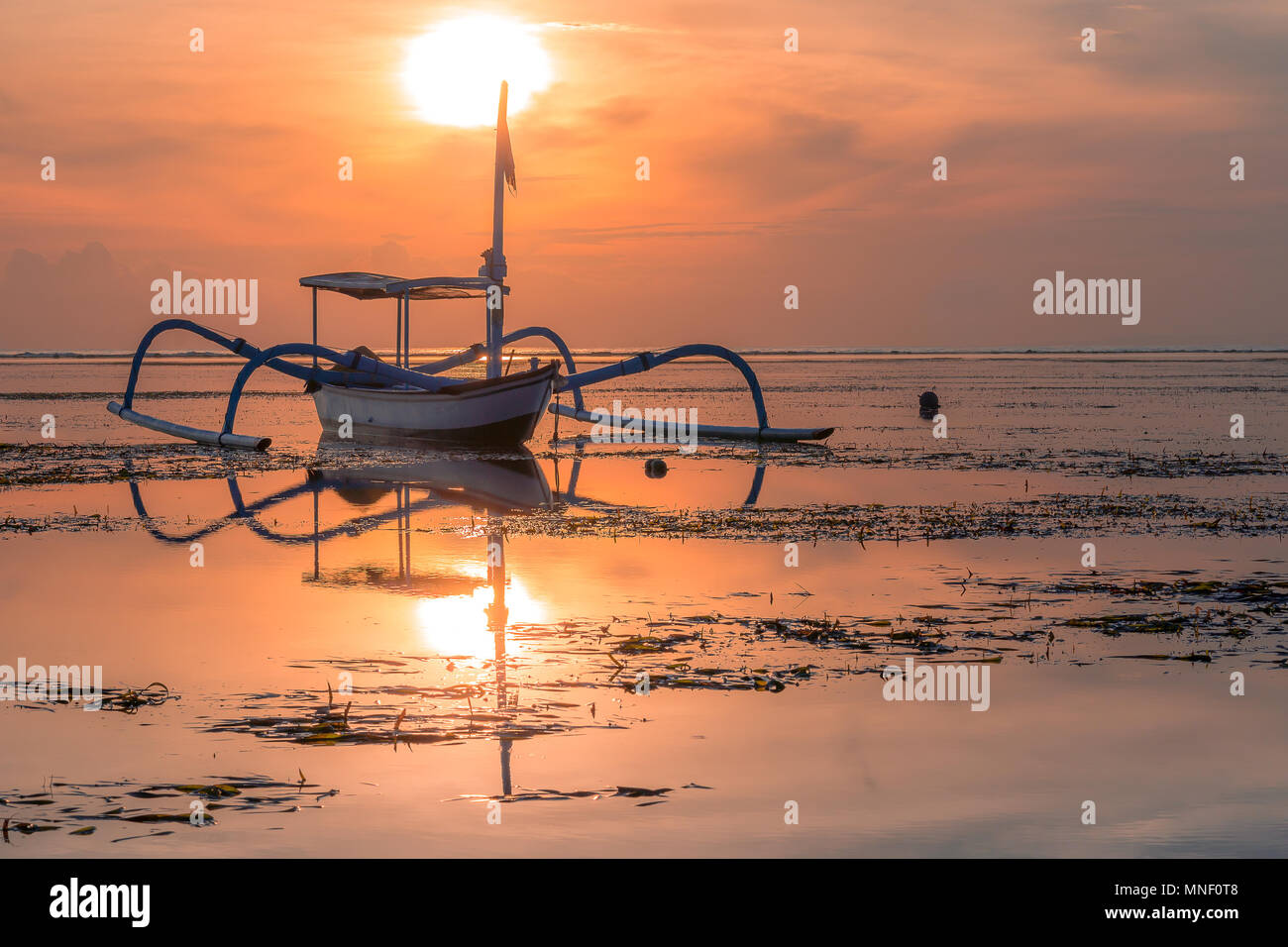 Un balinesian bateau de pêche au lever du soleil, les reflets dans la mer peu profonde, Sanur, Bali, Indonésie, 21 avril, 2018 Banque D'Images