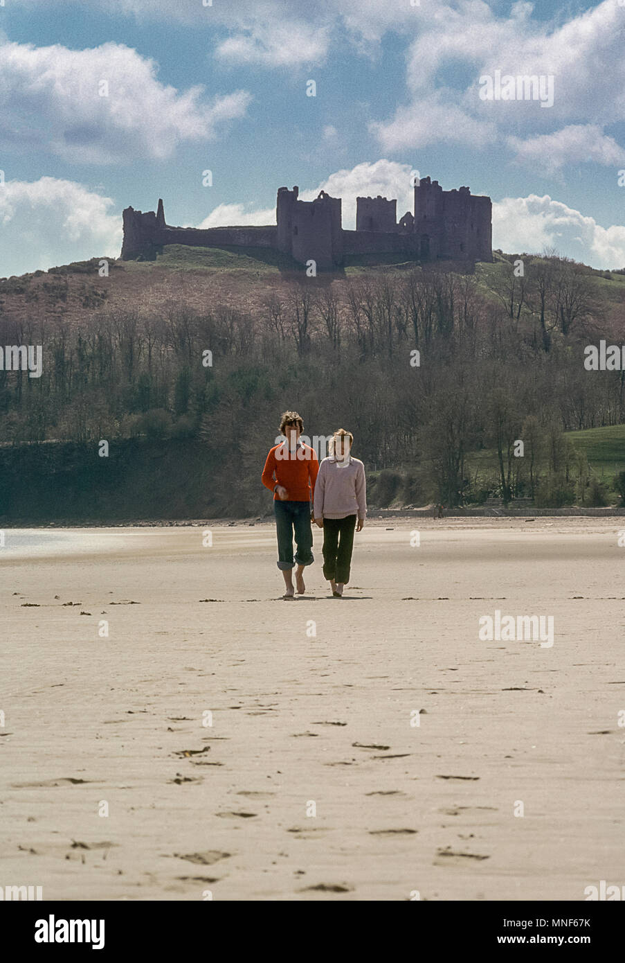 Jeune couple en train de marcher sur la plage en face de Llanstephan Castle dans Carmarthenshire, Pays de Galles, Royaume-Uni Banque D'Images