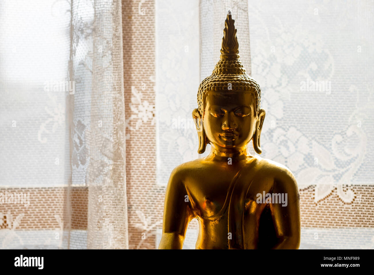 Statue de Bouddha en or silhouette presque s'asseoir à la fenêtre avec rideau blanc. Ménage de la Thaïlande de culte. Banque D'Images