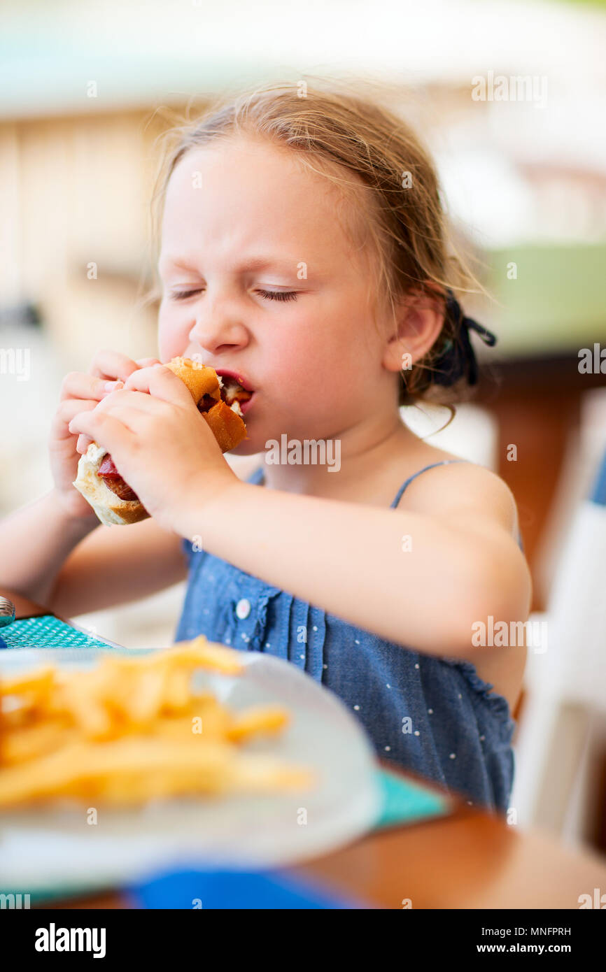 Adorable petite fille appréciant eating hot dog pour déjeuner au restaurant Banque D'Images