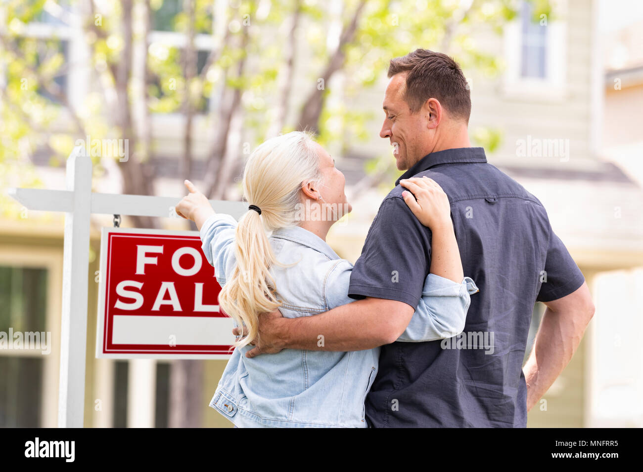Caucasian Couple confrontés et pointant vers l'avant de Achat Immobilier signe et maison. Banque D'Images