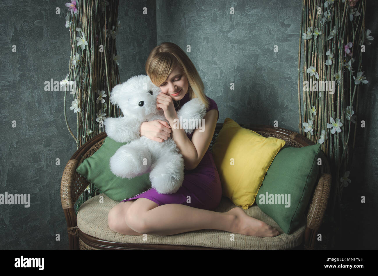 Portrait de fille mignonne en robe pourpre assis sur un canapé avec bear toy Banque D'Images