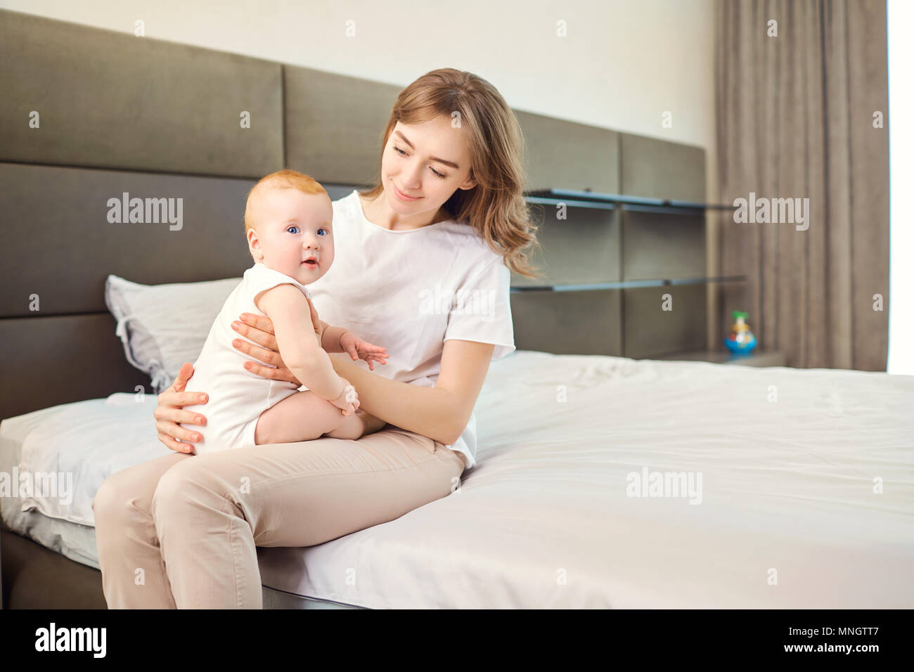 Maman et bébé sont assis sur le lit dans la chambre. Banque D'Images