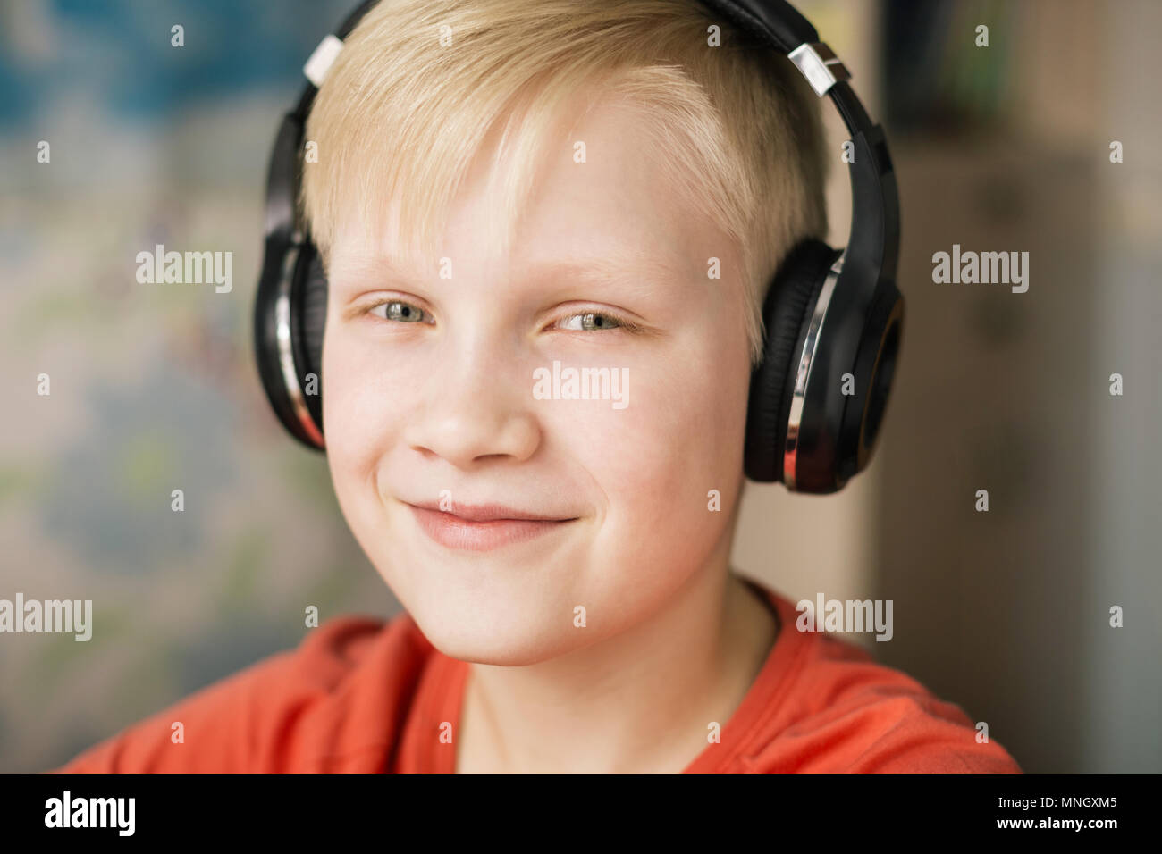 Blonde smiling boy à l'écoute de la musique dans les écouteurs, en souriant et en regardant la caméra. Banque D'Images