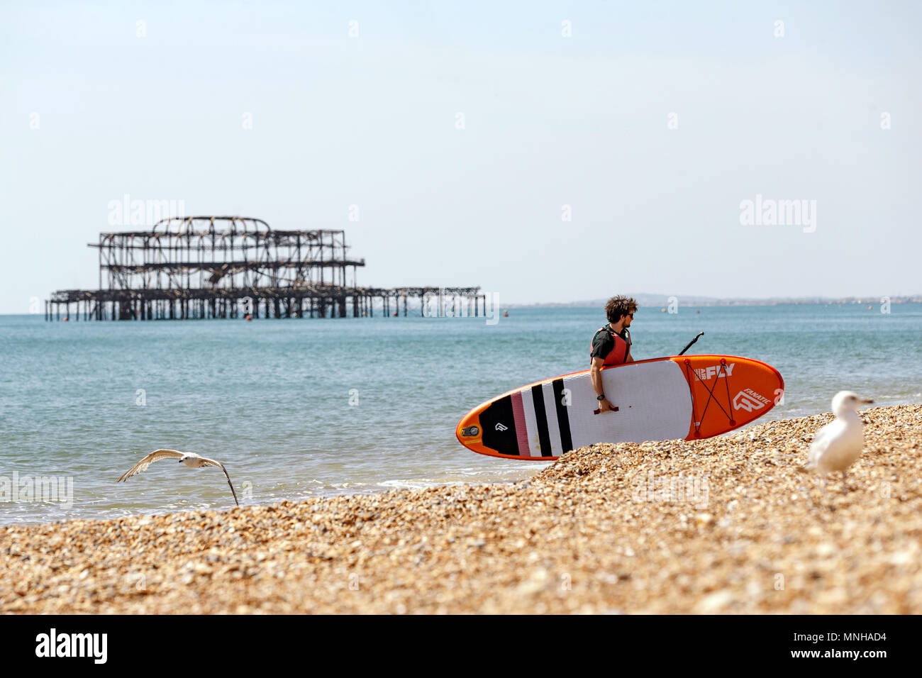 Un homme avec un surf ou paddleboard laissant la mer au cours d'une belle journée sur le front de mer de Brighton. Brighton, East Sussex, UK. Banque D'Images