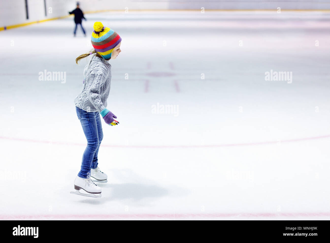 Adorable petite fille portant des jeans, pull-over chaud et coloré hat patinage sur glace Banque D'Images