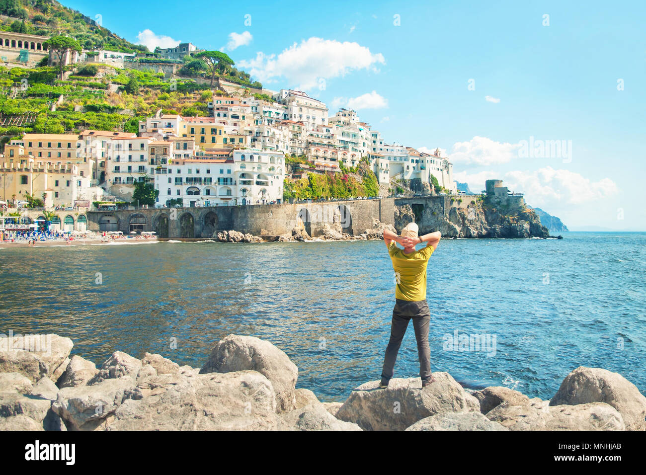 Young caucasian man standing sur les roches par la mer avec son dos à la caméra enjoying view de petite ville côtière européenne Banque D'Images