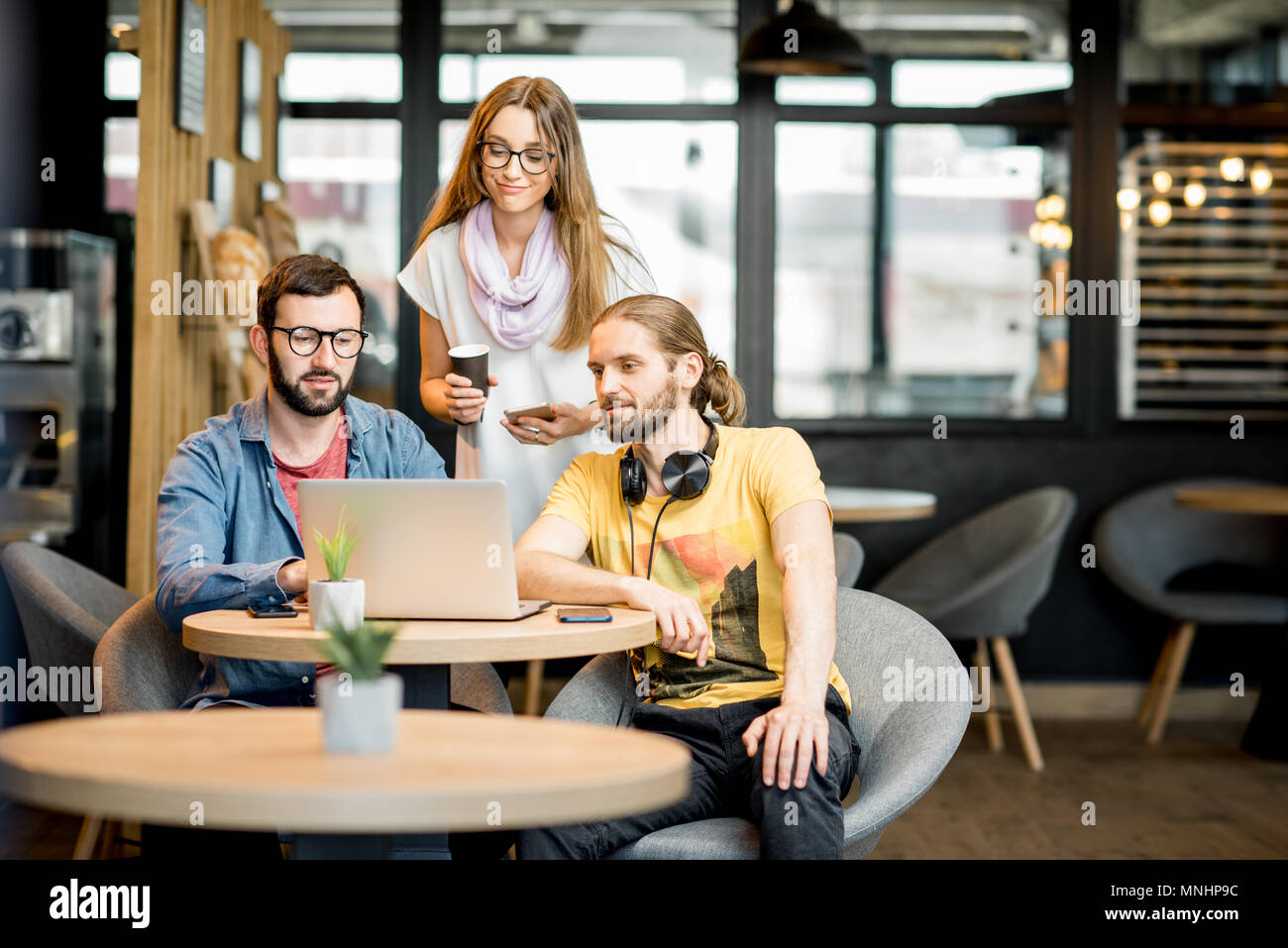 L'équipe de jeunes habillés de désinvolture qui travaillent ensemble avec un ordinateur portable pendant la pause café au café Banque D'Images