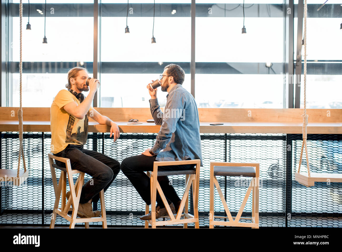 Deux amis habillés de désinvolture assis ensemble pendant la pause-café près de la fenêtre du café moderne Banque D'Images