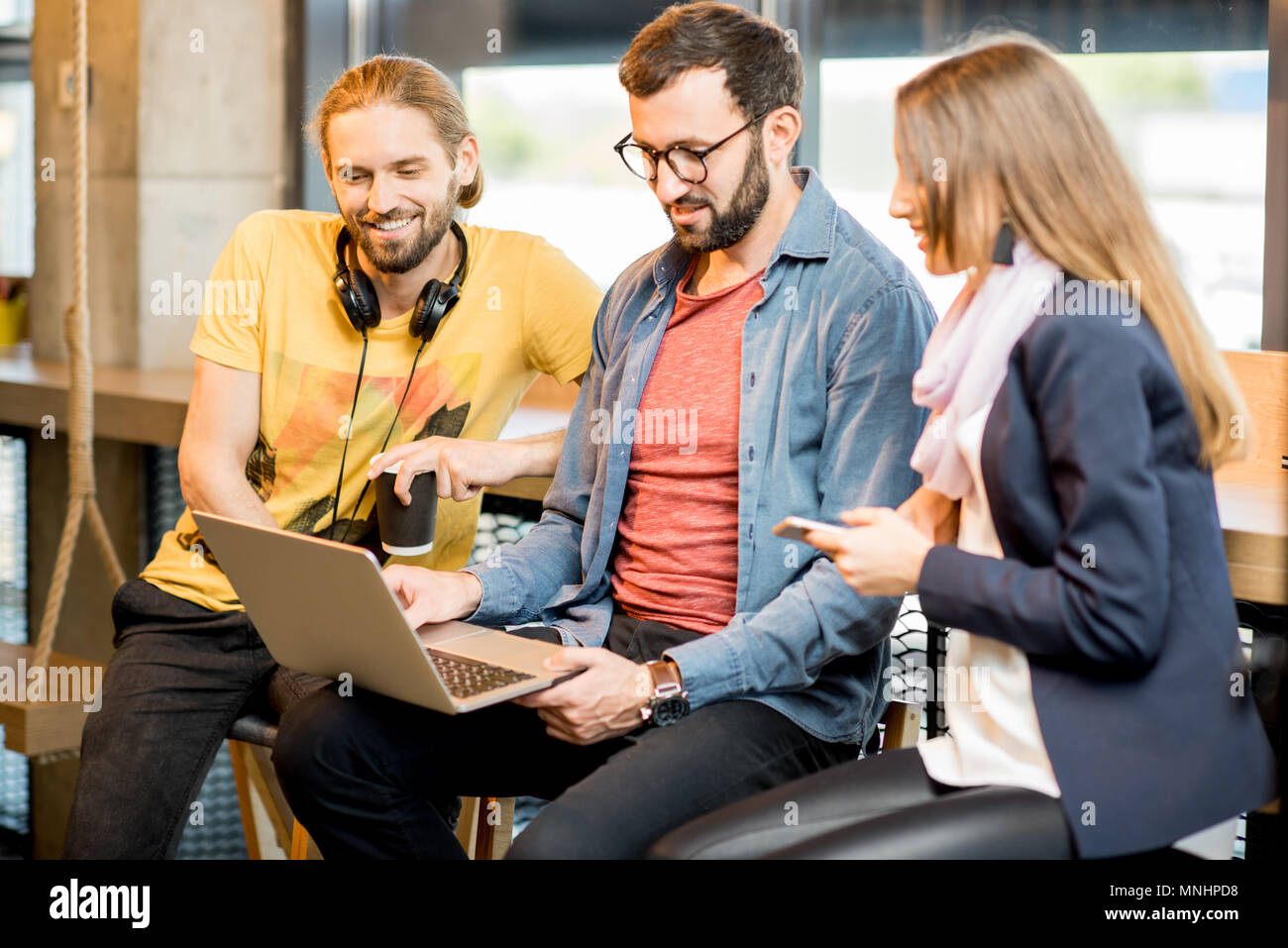 Jeunes collègues habillés à la légère le travail avec ordinateur portable assis ensemble dans le café Banque D'Images