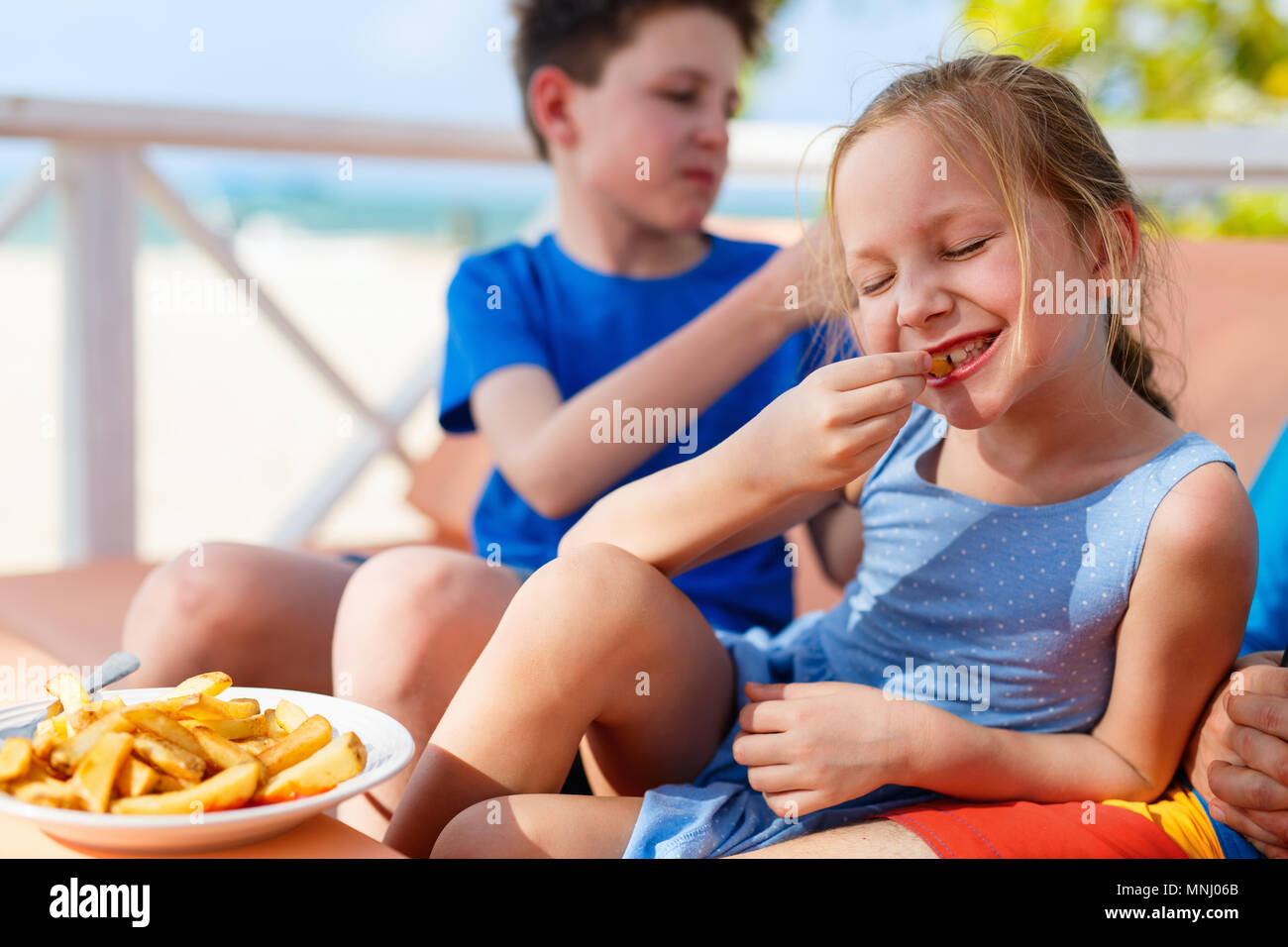 Adorable petite fille profiter de manger des frites avec son frère à l'extérieur restaurant sur journée d'été Banque D'Images