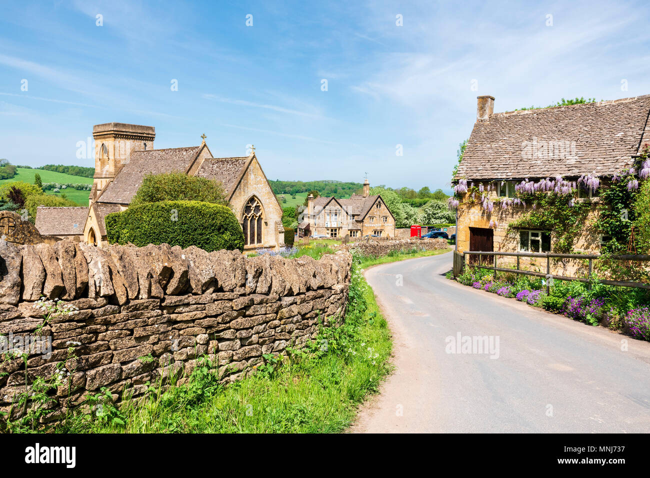 Snowshill, Cotswolds, en Angleterre, UK. Les fleurs de glycine sur un chalet à côté de l'église dans un village des Cotswolds. Banque D'Images