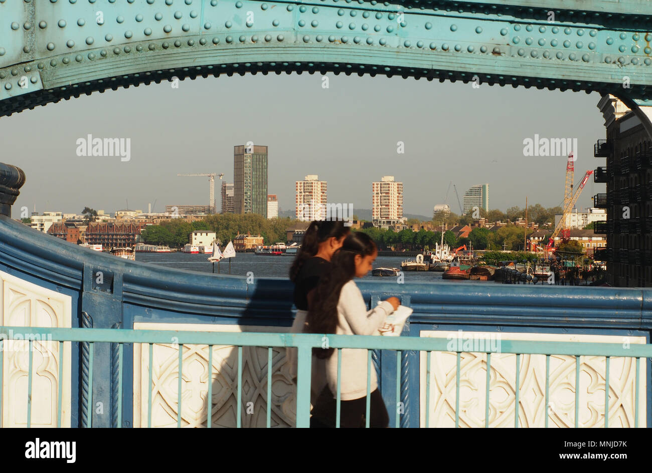 Deux jeunes femmes traversant le Tower Bridge, Londres à pied avec une vue vers l'Est de Londres sur une soirée ensoleillée avec des parties du métal du pont prend en charge Banque D'Images