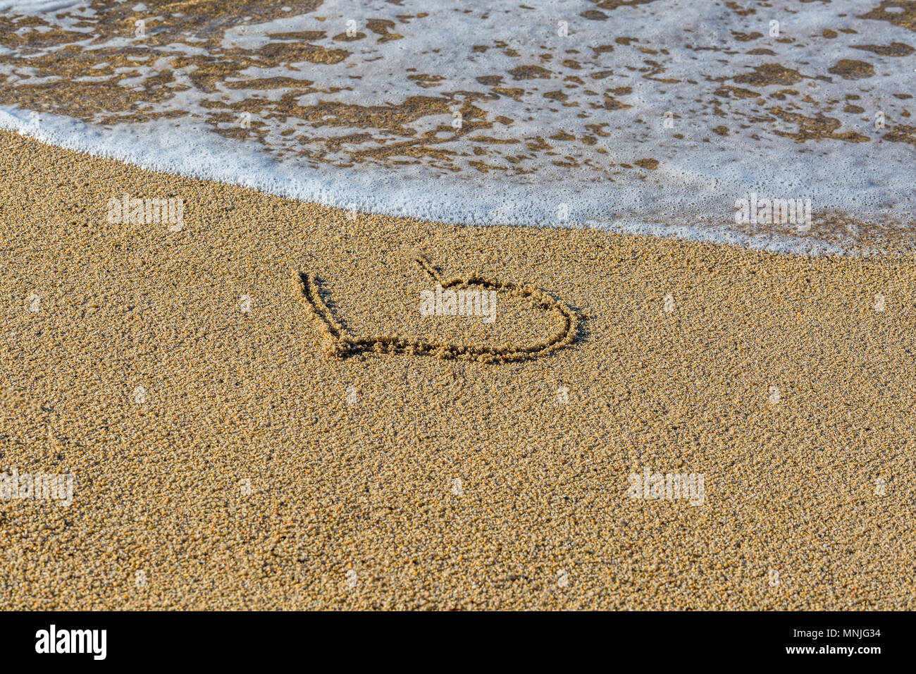 Coeur dessiné sur le sable humide. Une partie du coeur est emportée par une vague. Symbole du début ou de la fin de l'amour romantique. Vacances d'été concep Banque D'Images