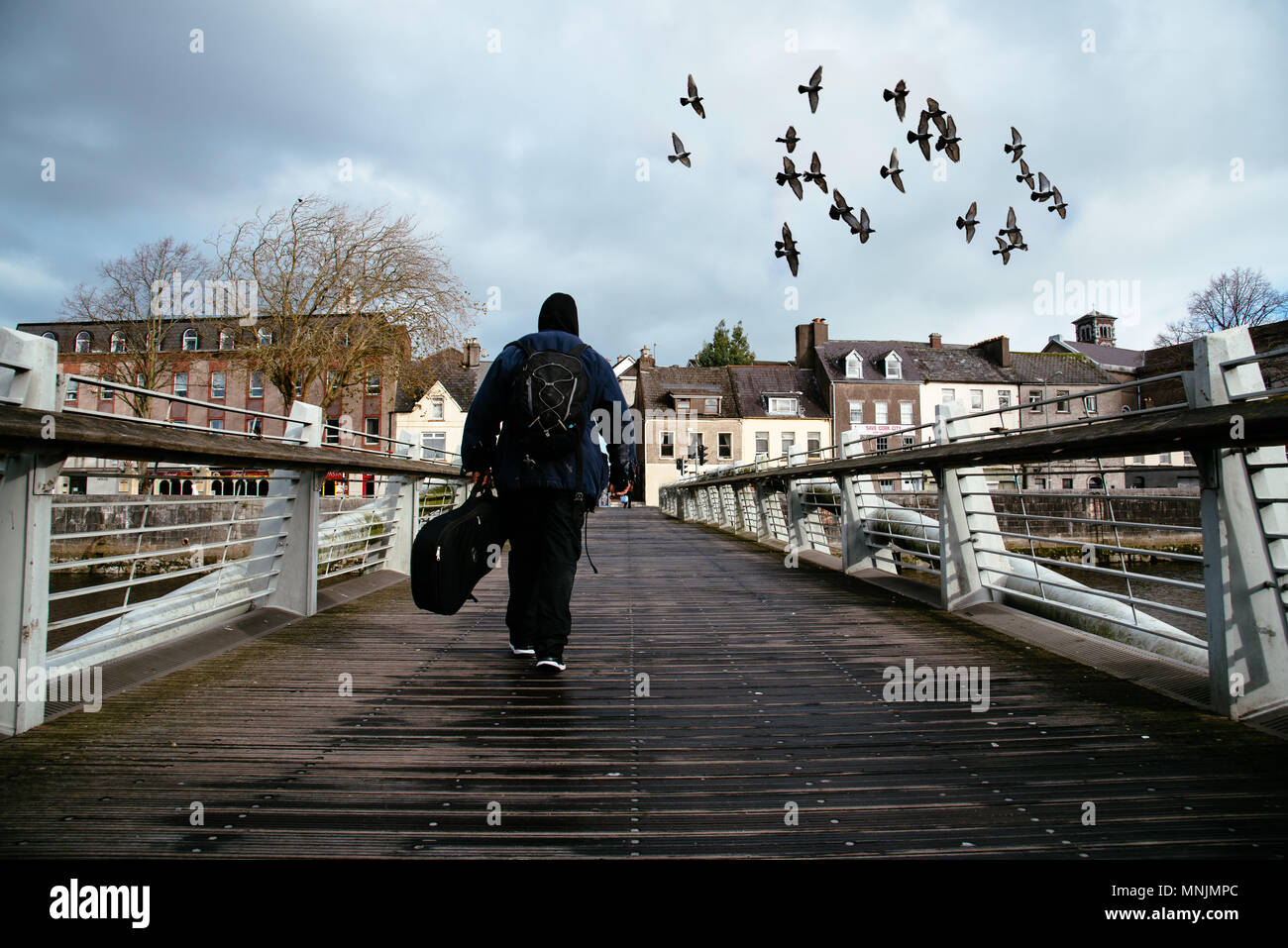 Mendiant tenant un instrument de musique de traverser un pont à Cork pendant qu'une nuée d'oiseaux s'envole au-dessus Banque D'Images