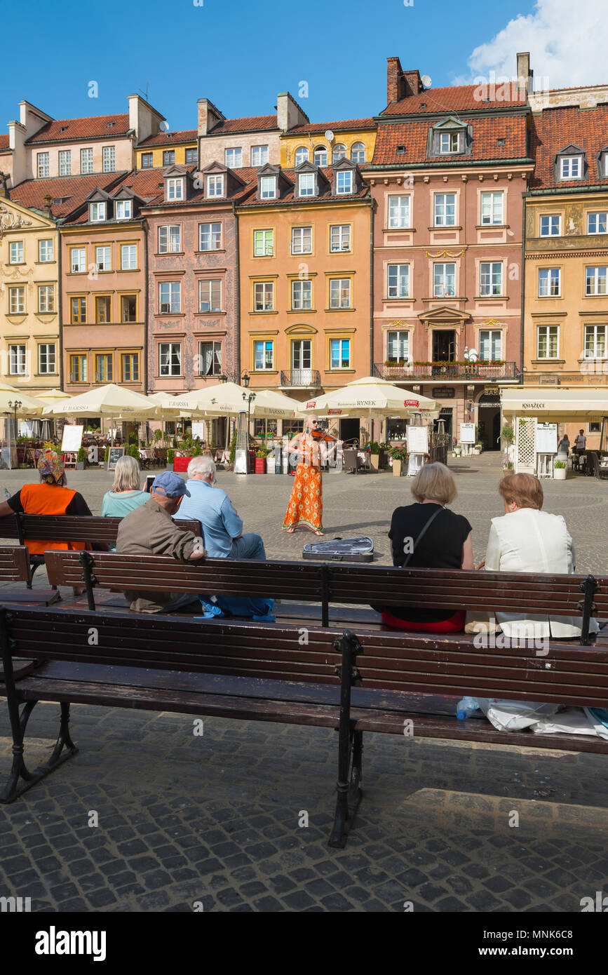 La vieille ville de Varsovie, un violoniste reçoit un groupe de personnes assises sur des bancs dans l'historique place de la vieille ville de Varsovie, Pologne. Banque D'Images