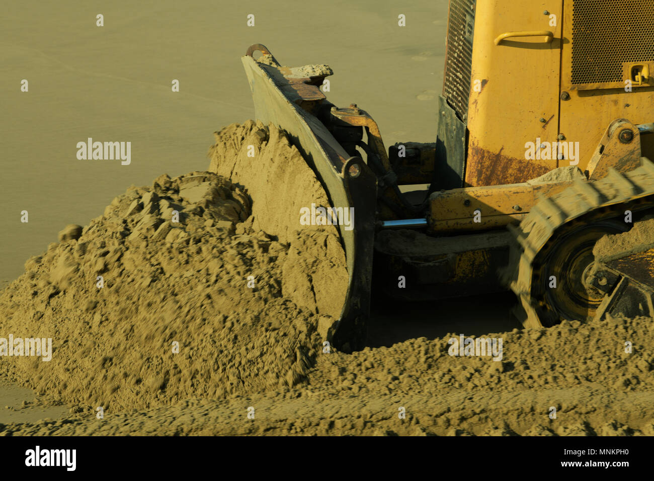 Close-up, détail, raclage bulldozer jaune sable humide, travaillant sur des projets de gestion des plages, flou Banque D'Images