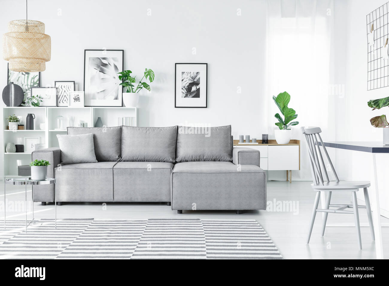 Salon scandinave intérieur avec un confortable canapé d'angle, des peintures, des plantes et des tapis à rayures Banque D'Images