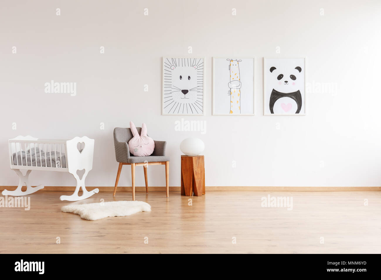 Dessins sur mur blanc gris au-dessus de chaise avec oreiller et banc de bois dans la chambre de bébé avec berceau blanc et tapis Banque D'Images