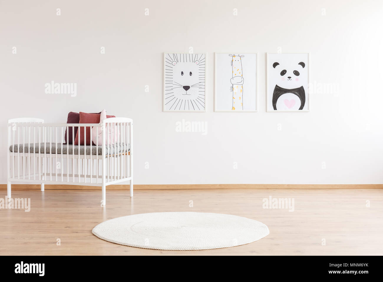 Tapis rond blanc à côté du lit d'enfant avec des oreillers contre mur blanc avec des affiches et copy space Banque D'Images