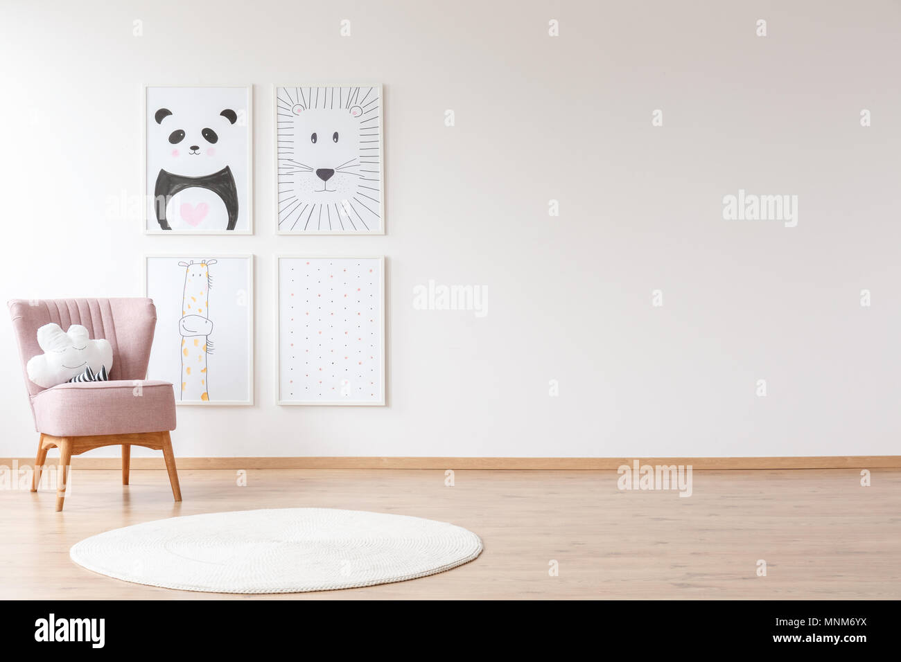 Fauteuil avec coussin rose et blanc tapis rond dans la chambre de bébé avec des affiches sur un mur avec copie espace Banque D'Images