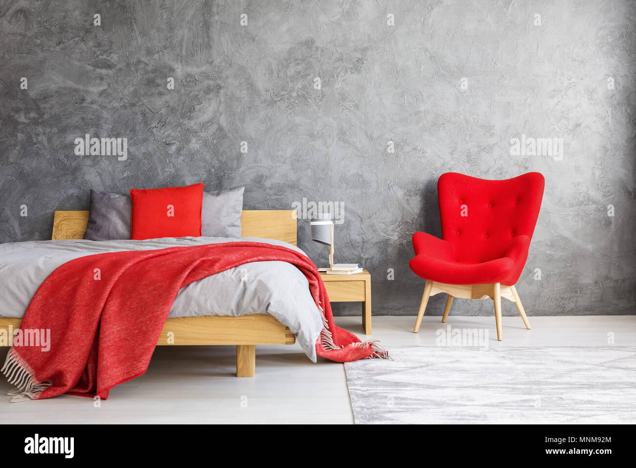 Fauteuil rouge debout à côté de lit avec oreillers et couvre-lit dans chambre spacieuse avec mur vide Banque D'Images