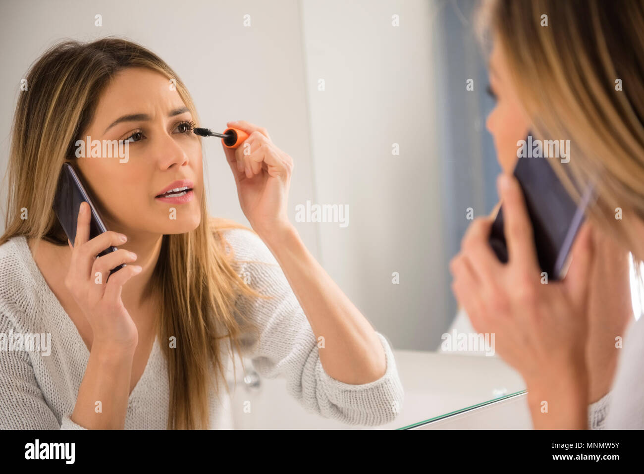 Jeune femme à l'aide de smart phone et le mascara Banque D'Images Jeune femme à l'aide de smart phone et le mascara Banque D'Images