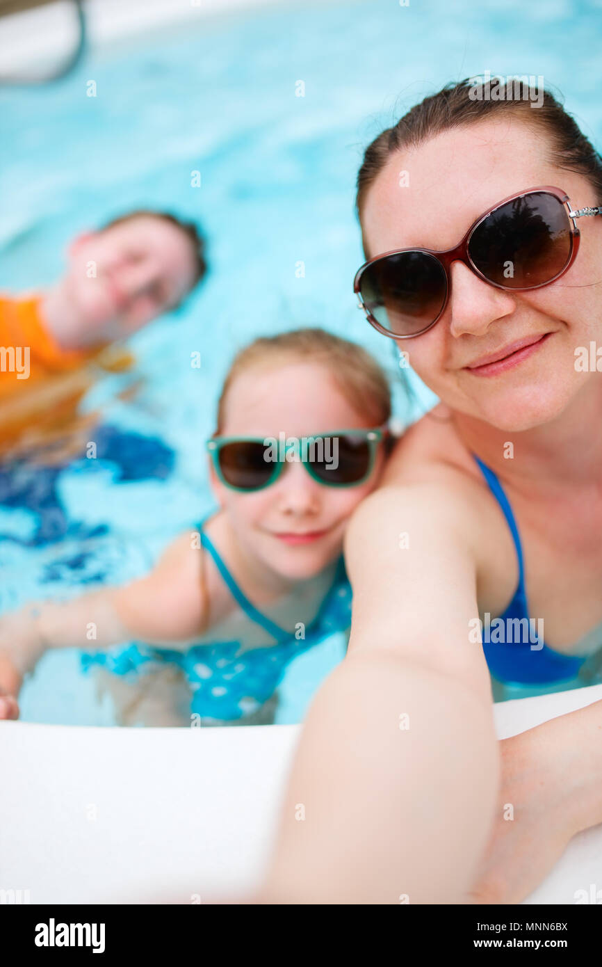 Mère de famille heureuse et ses enfants à l'extérieur piscine en tenant sur selfies vacances tropicales Banque D'Images