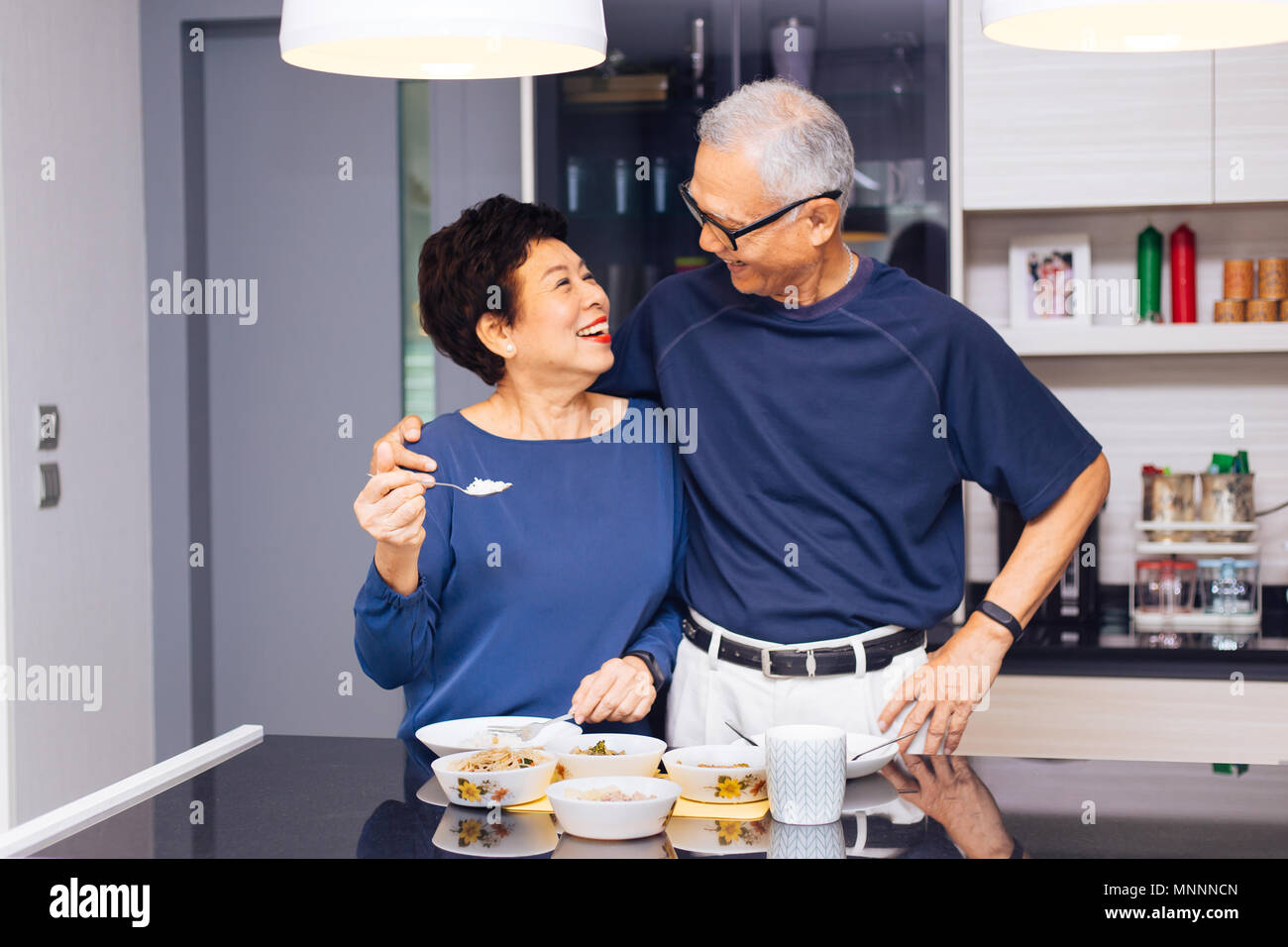 Senior Asian couple de grands-parents ensemble pendant que la cuisson des aliments est l'alimentation de la femme à l'homme à la cuisine. Relation durable concept Banque D'Images