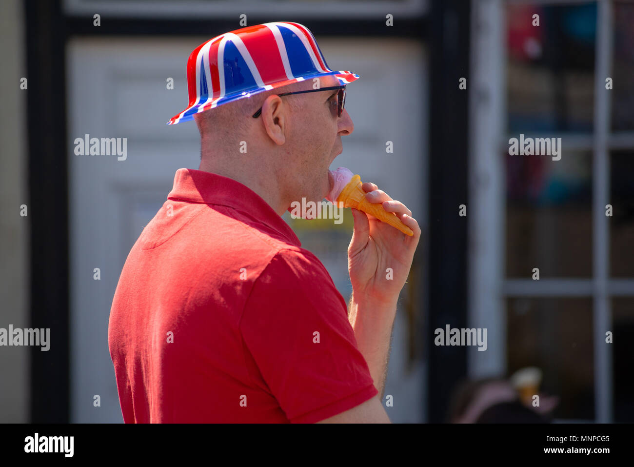 Un homme portant un chapeau de Union Jack et mangeant une glace à une projection de rue du mariage royal du prince Harry et de Meghan Markle. Ringwood, Hampshire, Angleterre, Royaume-Uni, 19th mai 2018. Banque D'Images