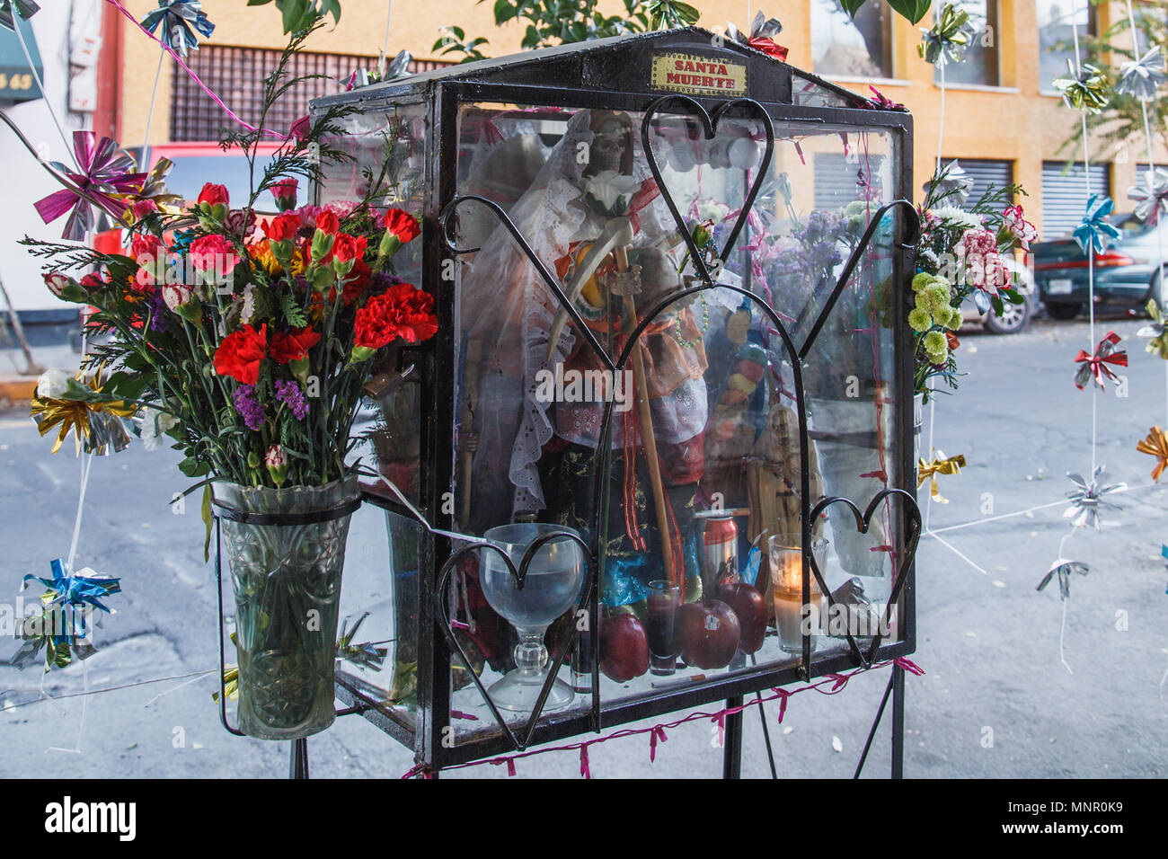 Un sanctuaire de Santa Muerte dans la rue, c'est réuni avec des fleurs fraîches, fruits,une bougie, de l'eau et des ornements colorés, Mexico, Mexique. Banque D'Images