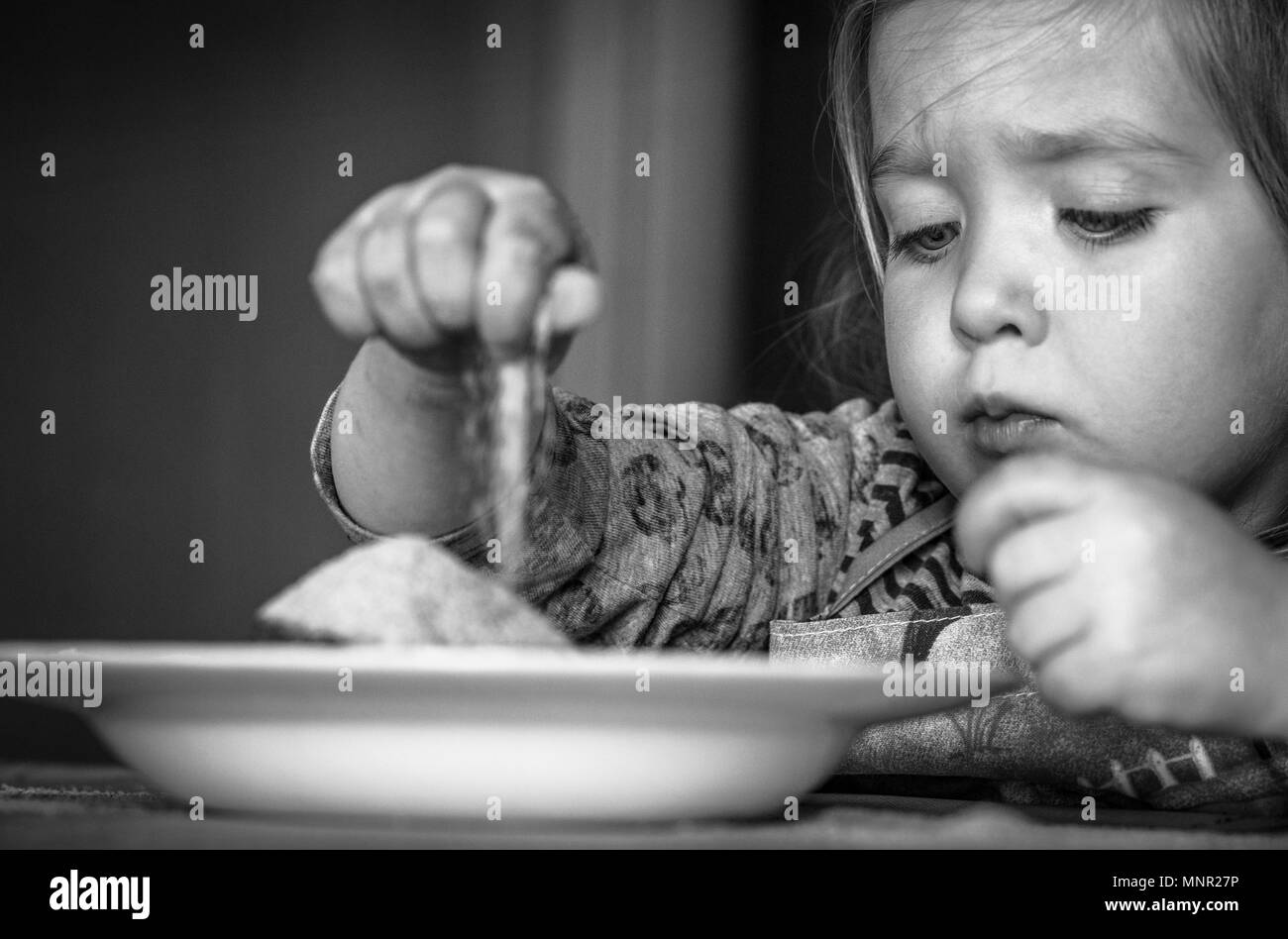 Deux ans et demi (fille) enfants jouant avec une assiette pleine de nourriture (sucre) en noir et blanc Banque D'Images