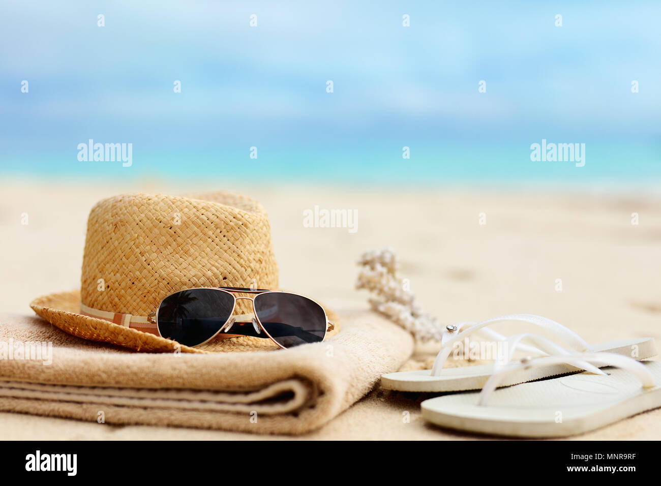 Chapeau de paille, serviette, lunettes de soleil et tongs sur une plage tropicale Banque D'Images
