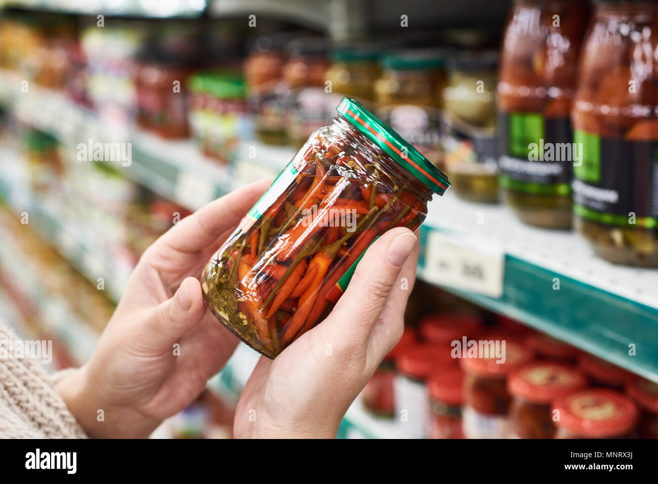 Les mains de l'acheteur avec un peut de conserves de piments rouges dans le magasin Banque D'Images