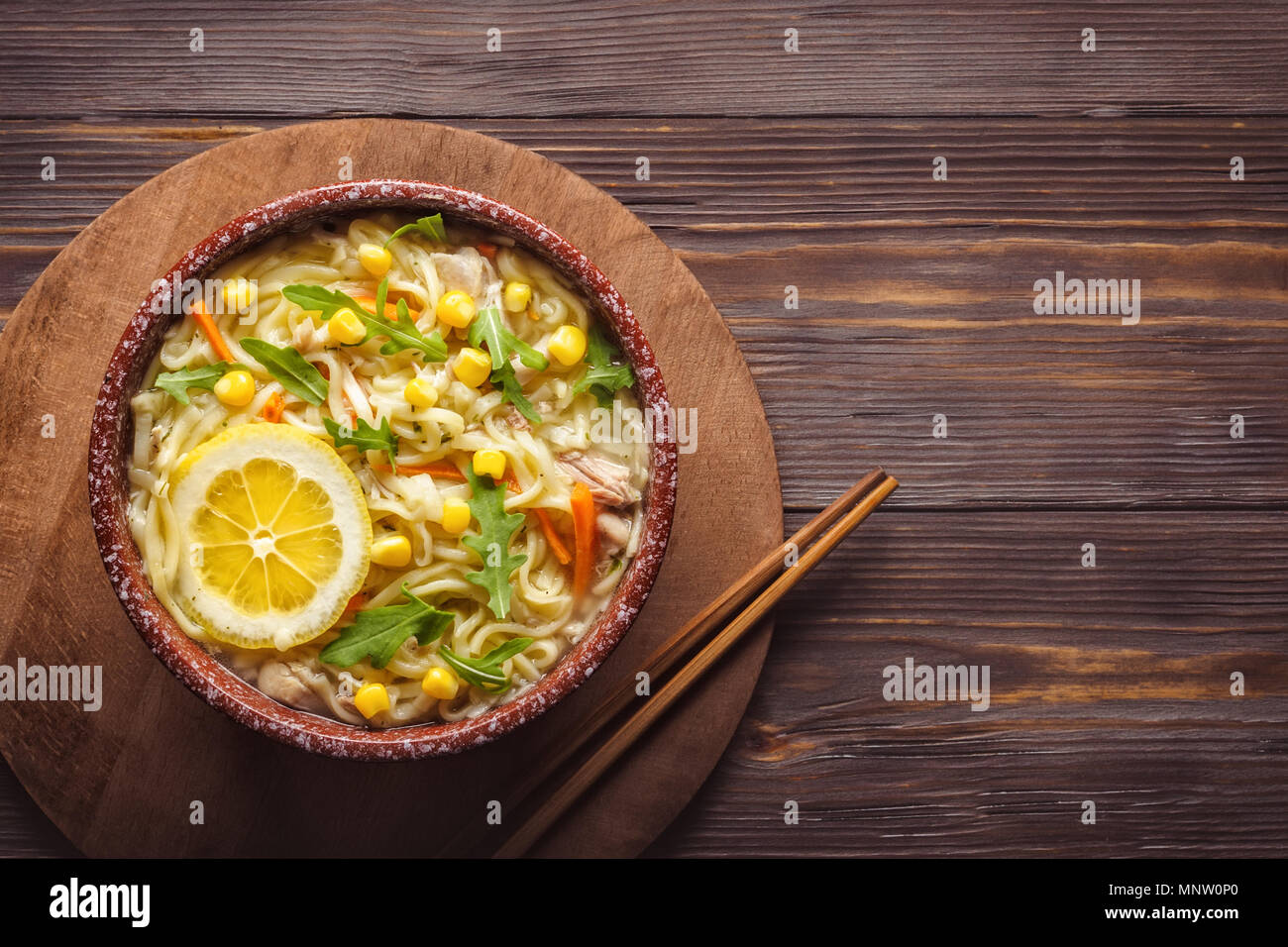 La nourriture asiatique soupe chinoise aux vermicelles dans un bol de légumes verts Oignons Carottes roquette feuilles du maïs et de la viande de poulet style baguettes Wabi Sabi clé faible Banque D'Images