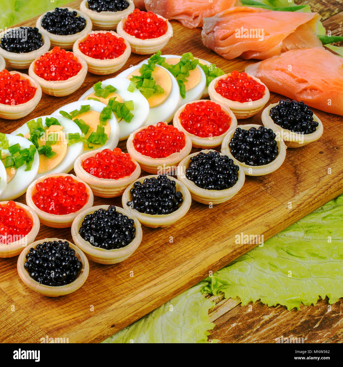 Des tartelettes avec du caviar rouge et noir, le saumon, la laitue et les oeufs. Sur une planche à découper. Concept d'aliment de luxe. Square. Close-up. Banque D'Images