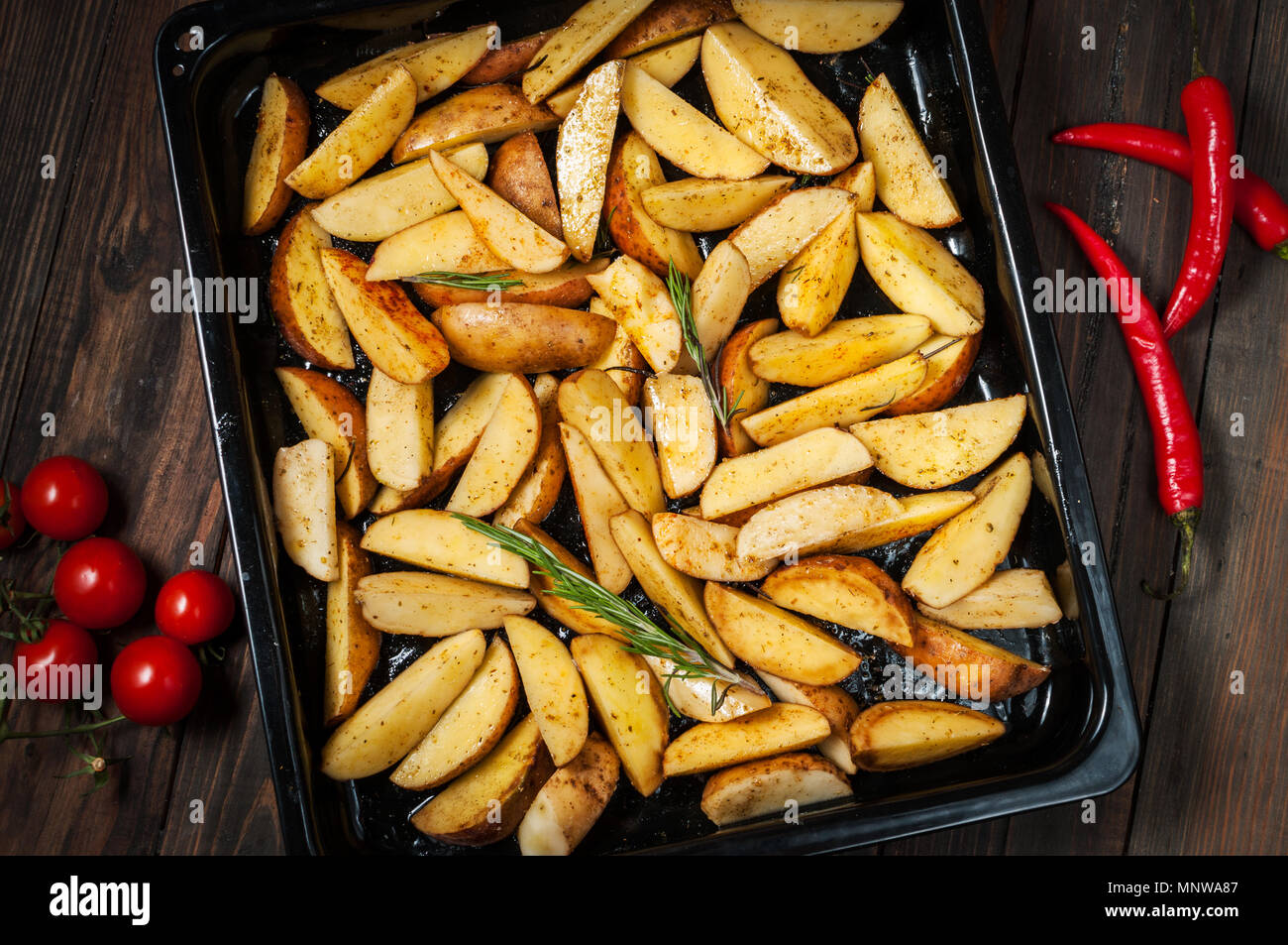 Quartiers de pommes de terre non cuites avec le romarin et le poivre. Banque D'Images