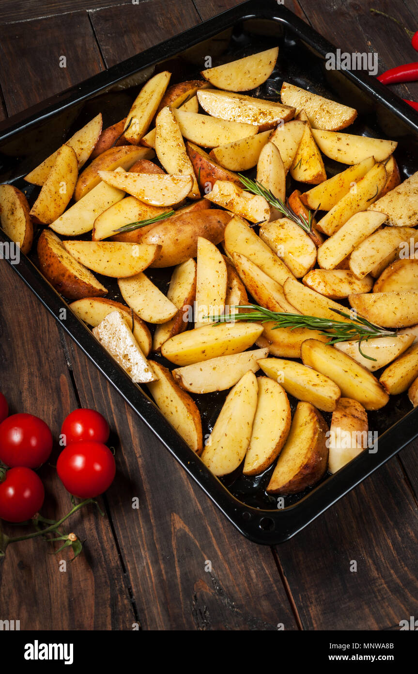 Quartiers de pommes de terre non cuites avec le romarin et le poivre. Banque D'Images