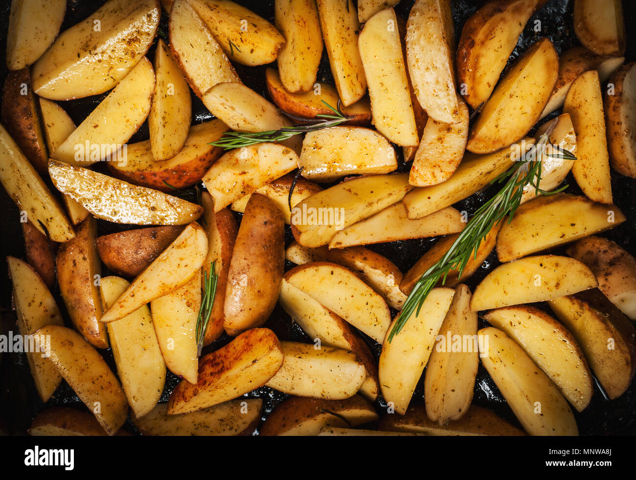 Quartiers de pommes de terre non cuites avec le romarin et le poivre. Banque D'Images