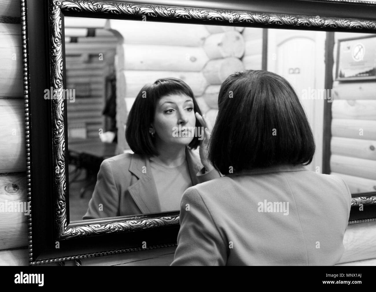 Une jeune femme regarde son reflet dans le miroir. Photo en noir et blanc. Banque D'Images