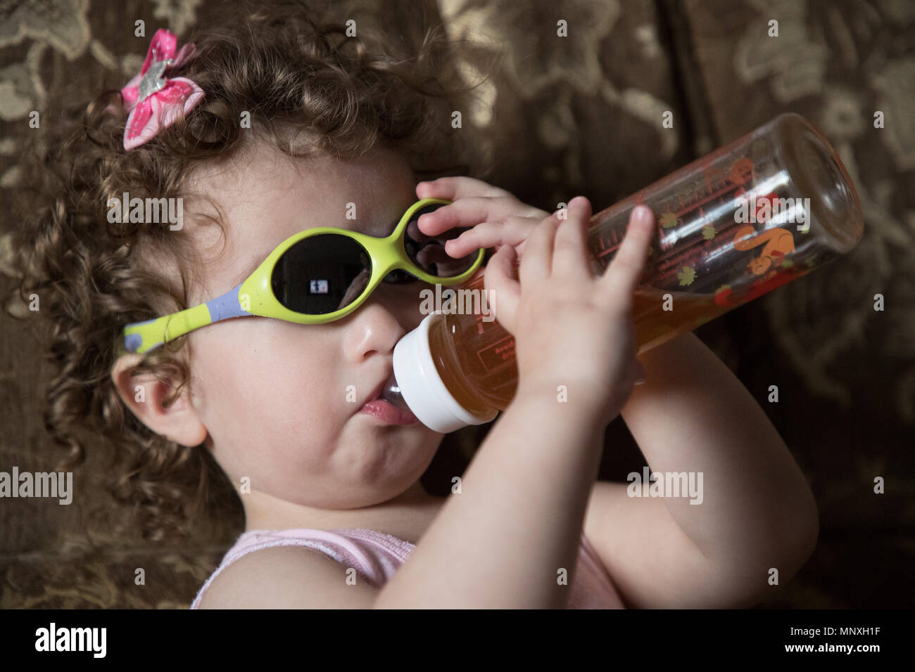 Petit enfant dans un verre de lunettes de jus d'un bouteille en plastique pour enfants Banque D'Images