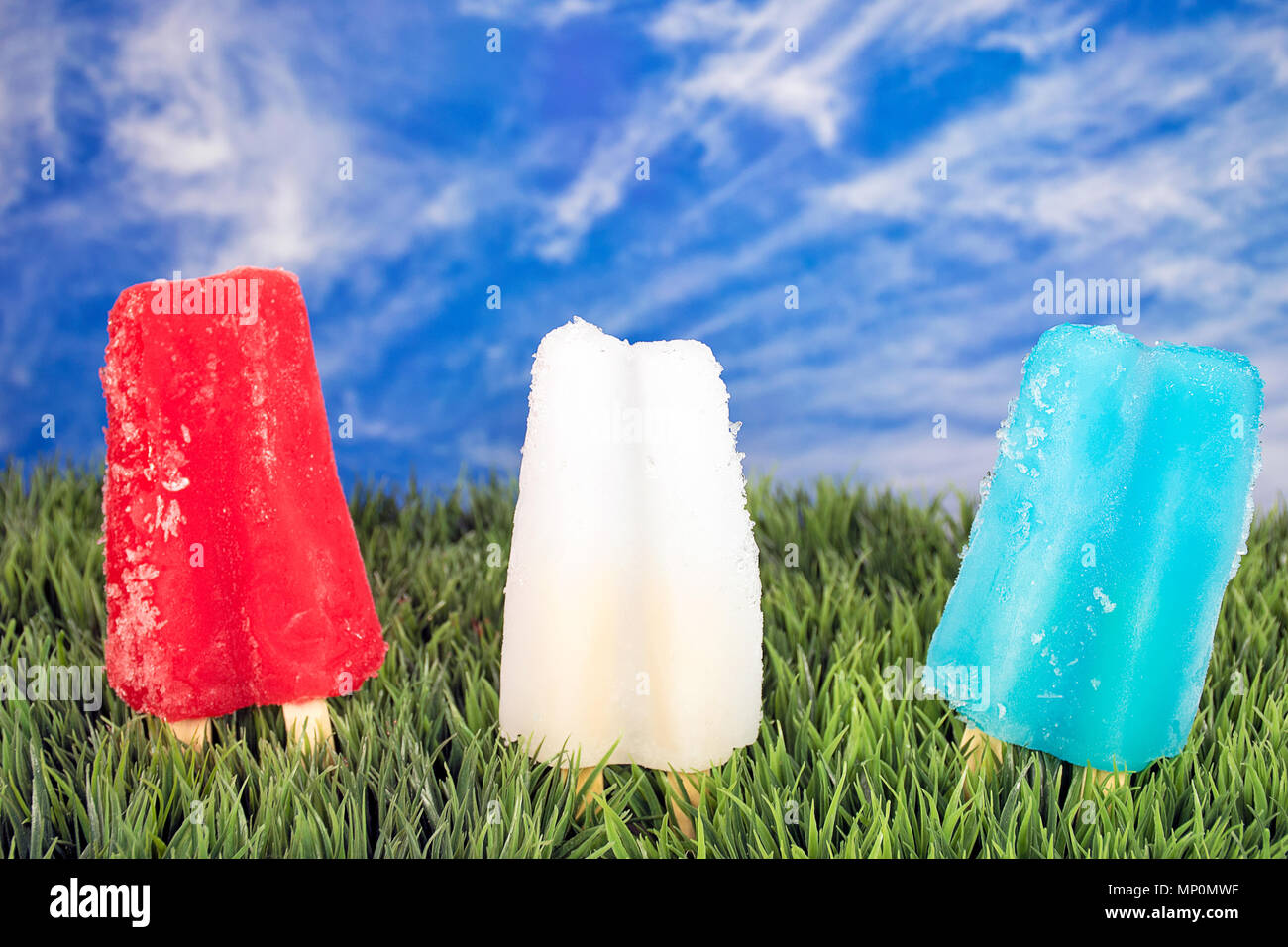 Rangée de rouge blanc et bleu les sucettes glacées dans l'herbe avec fond de ciel d'été Banque D'Images