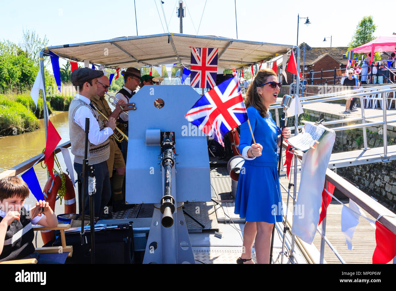 Salut à la 40s populaire événement nostalgique. La victoire de guerre groupe jouant sur pont de bateau, avec des profils femme chantant et agitant le drapeau Union Jack. Banque D'Images