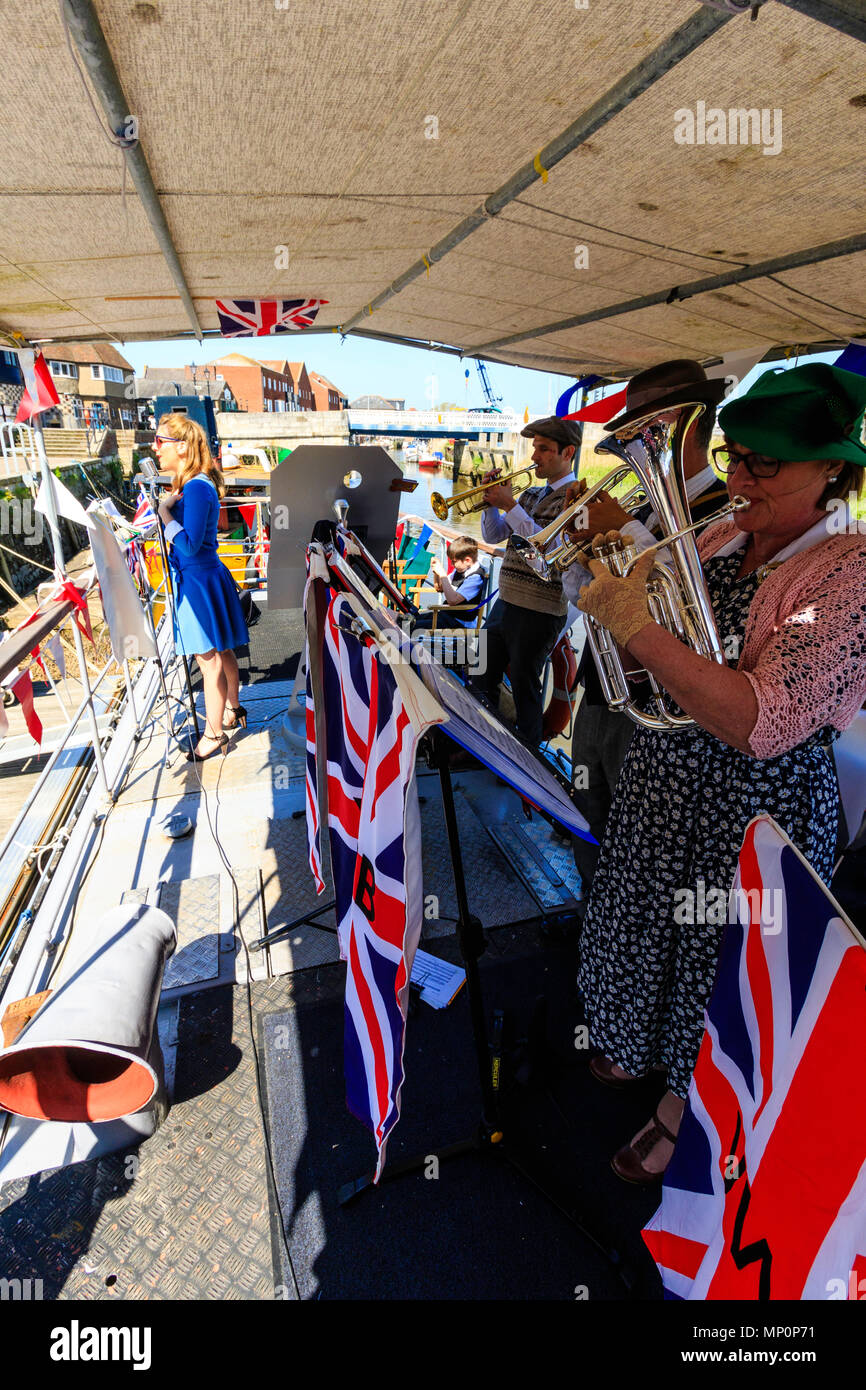 Salut à la 40s populaire événement nostalgique en Angleterre. La victoire de la bande de guerre et une femme sur scène chanteuse pont de bateau avec l'Union jack drapeaux. Banque D'Images