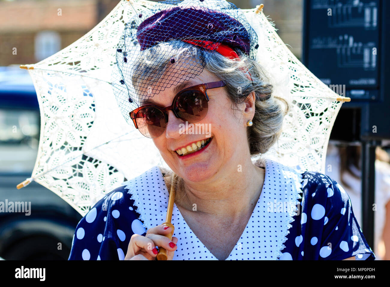 Salut à la 40s populaire événement nostalgique. Tête et épaules, smiling middle-aged woman with 40's période vêtements, tenant un parasol. Eye-contact. Banque D'Images