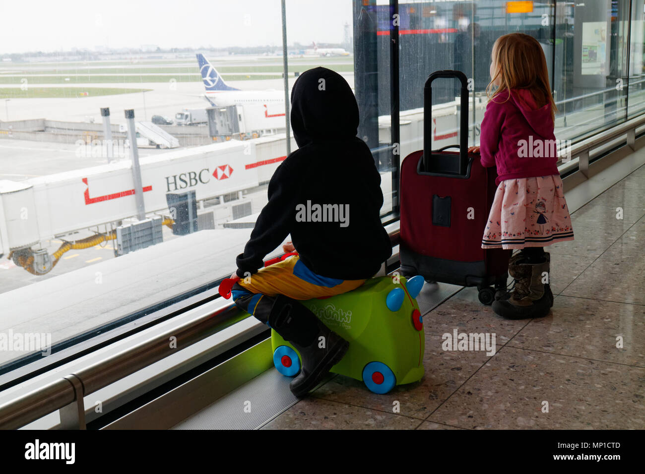 Deux enfants (5 et 3 ans, frère et sœur) avec leurs valises en regardant par la fenêtre à l'aéroport Heathrow de Londres Banque D'Images