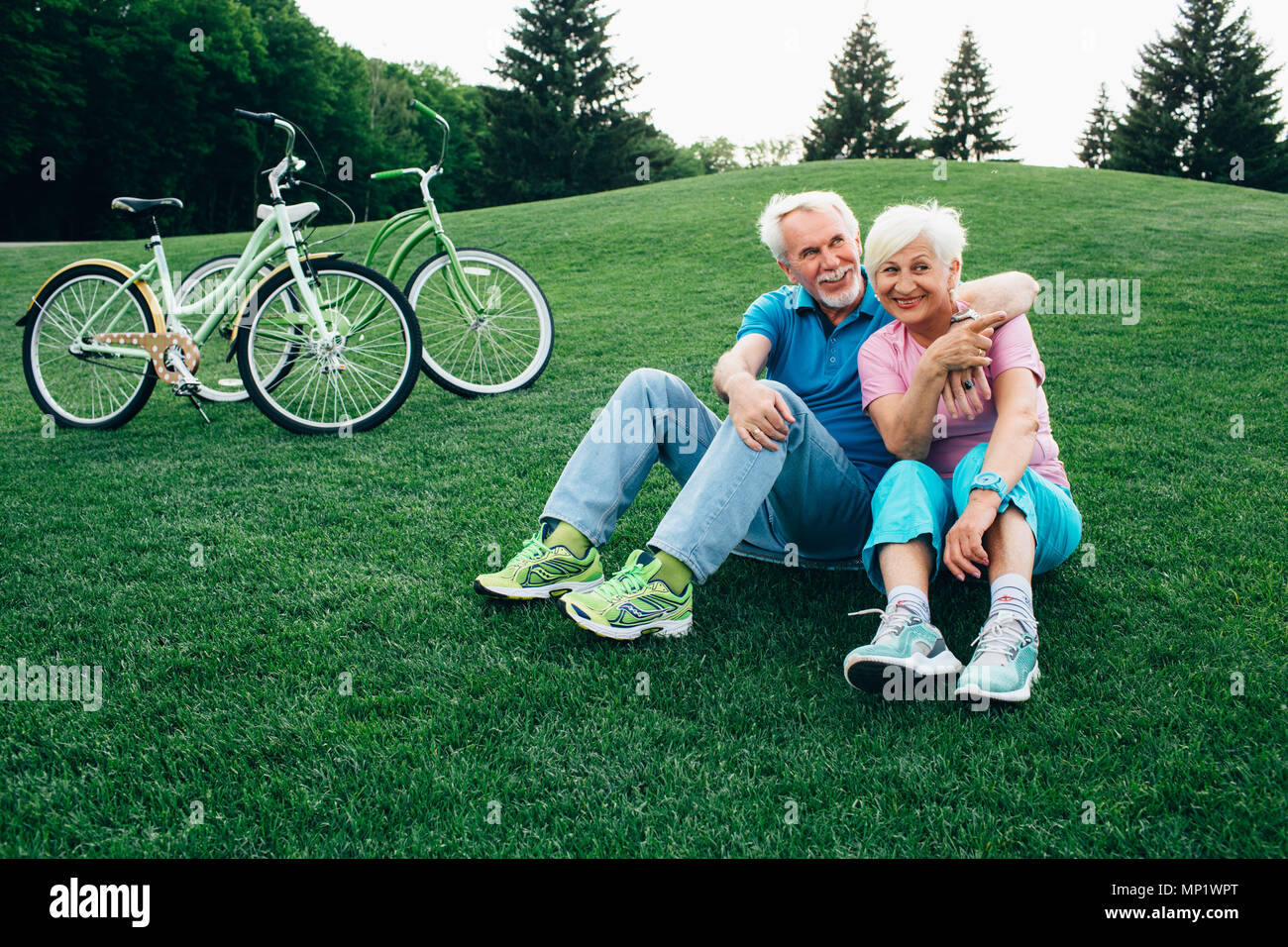 Happy senior couple est assis sur l'herbe, profiter le reste après la bicyclette. Stand des vélos à côté d'eux. Le repos actif des personnes âgées, Banque D'Images