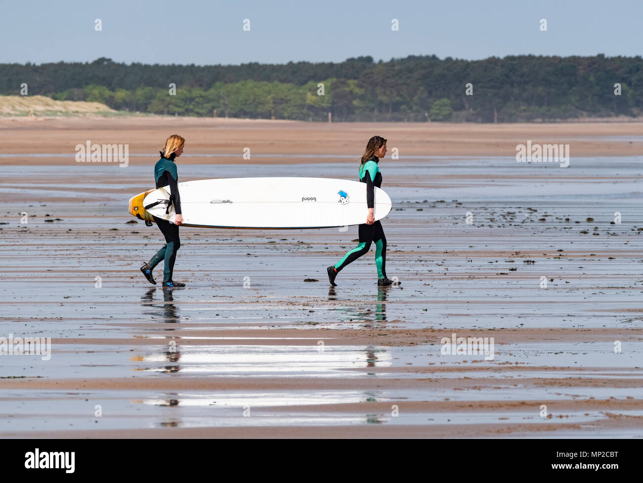 Deux femmes portent des planches de surf de mer à Belhaven Beach, East Lothian, Ecosse, Royaume-Uni Banque D'Images